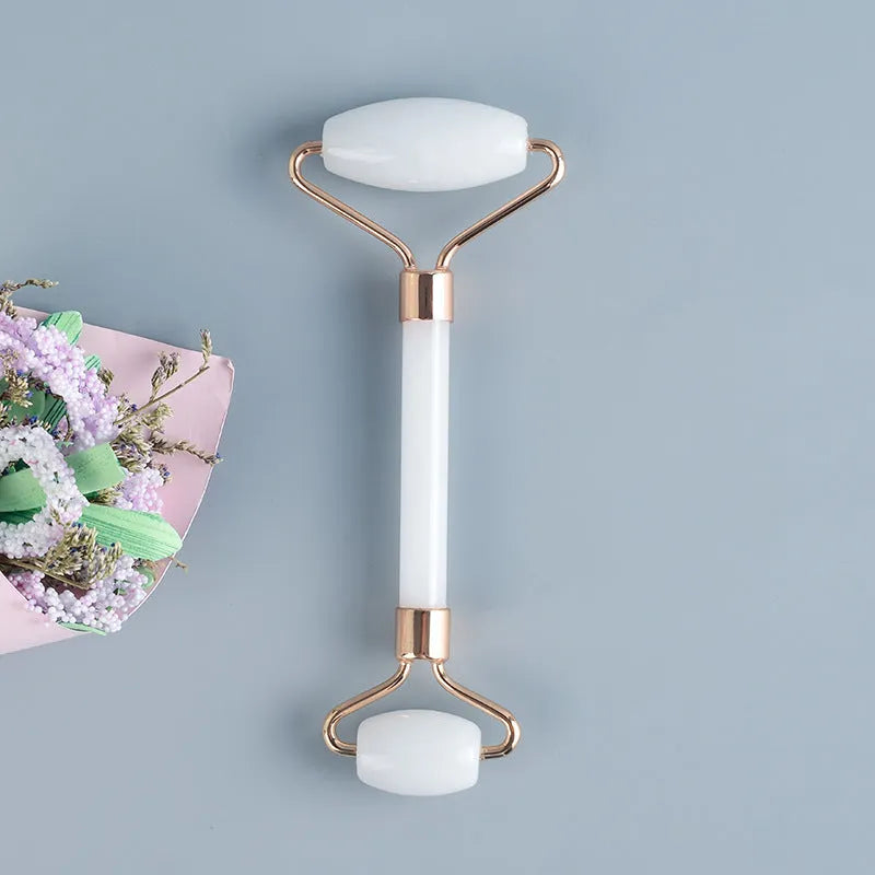 White jade facial roller and gua sha board set on a plain surface.