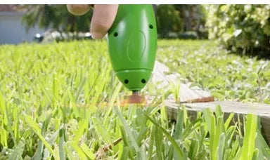Cordless handheld lawn trimmer with extension pole and protective debris shield on a lawn.
