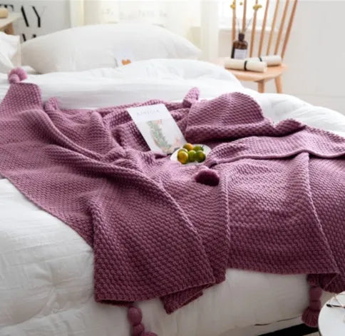 Nordic style fringed knit throw blanket in a neutral colour, shown draped over a sofa.