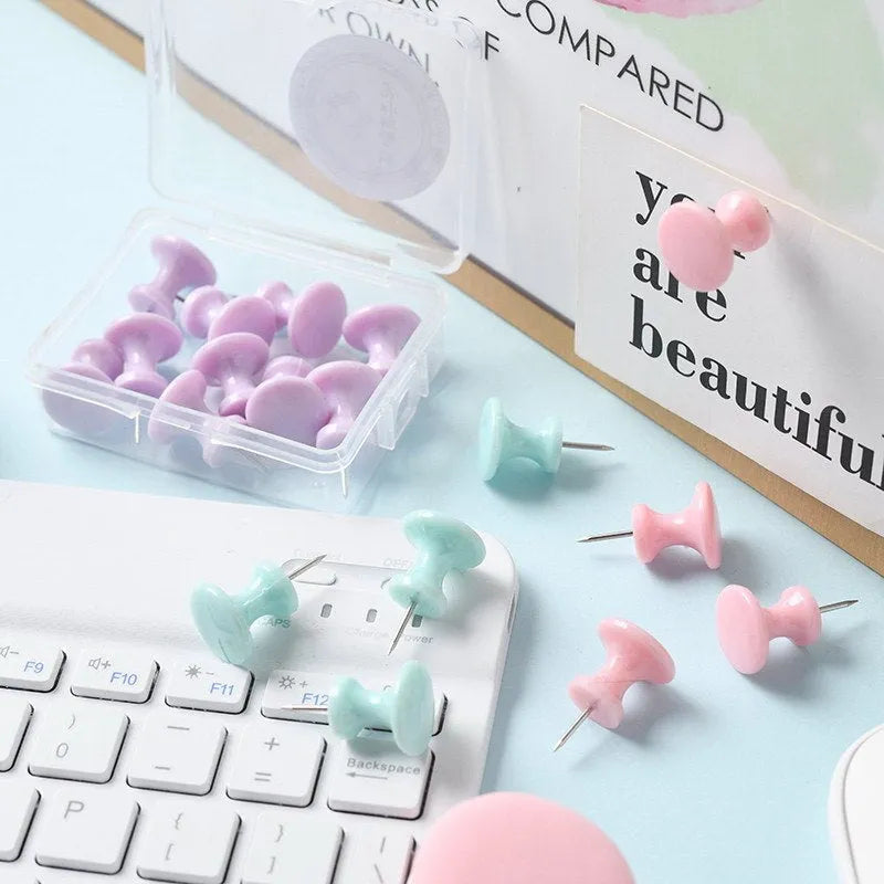 Box of coloured plastic push pins in cherry blossom pink, mint green and lavender on a white surface