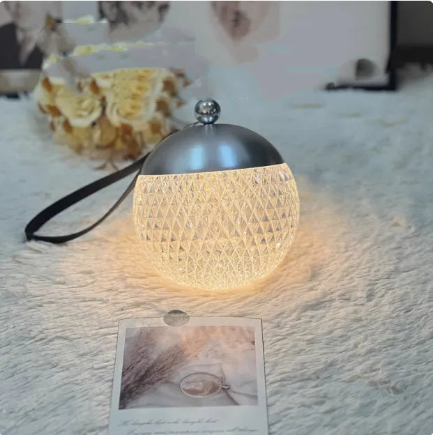 Small round touch-control dimmable LED night lamp in a metallic finish on a wooden table.