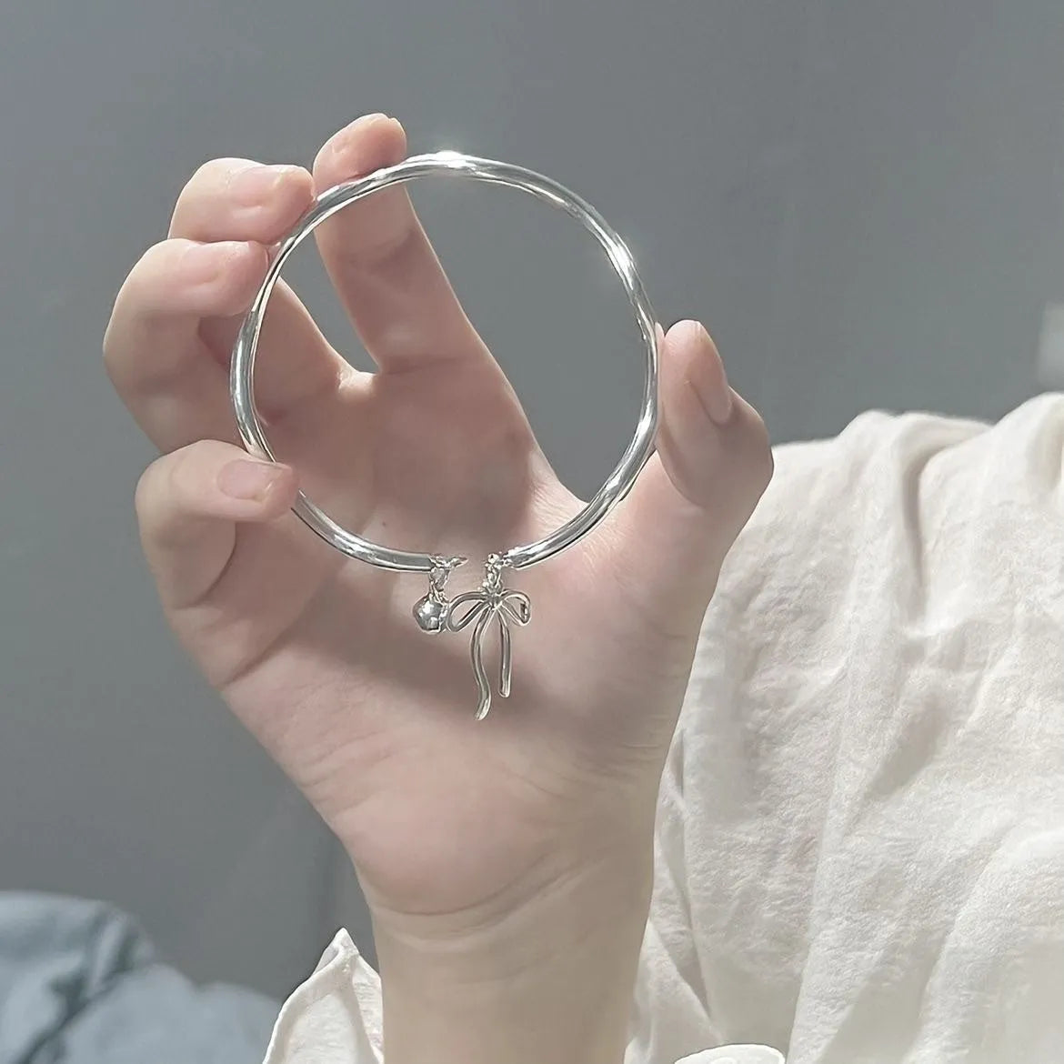 Silver bow adjustable bracelet with bell opening mechanism on wrist
