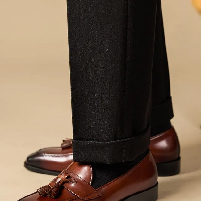 Men's black polished leather tassel loafers on a white background, side view showing rubber sole.