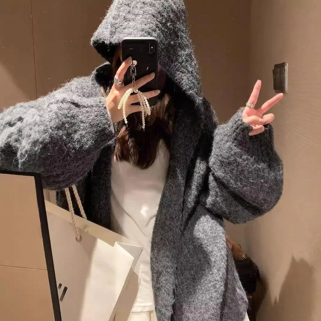 A woman's loose-fit hooded sweater cardigan in a thick fabric, shown in dark grey, brown, and milky white colour options.