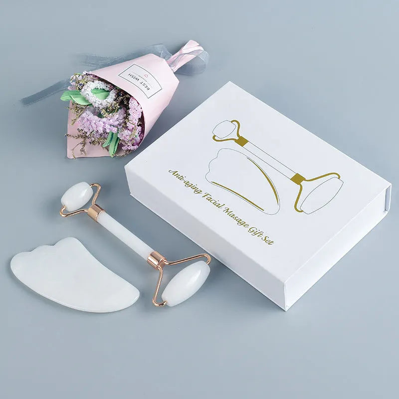 White jade facial roller and gua sha board set on a plain surface.