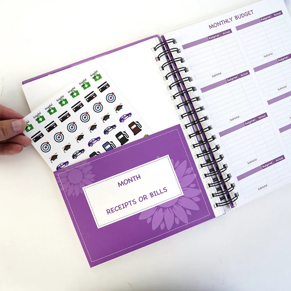 Purple coil-bound budget planning notebook with pen, stickers, and paper clips for financial organisation