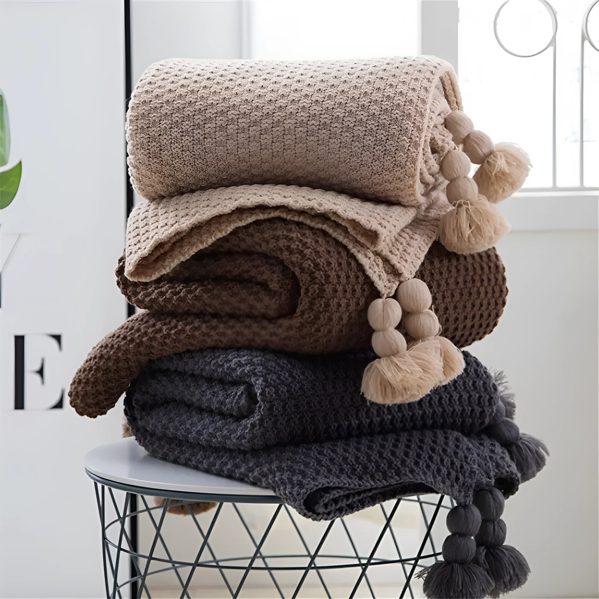 Nordic style fringed knit throw blanket in a neutral colour, shown draped over a sofa.
