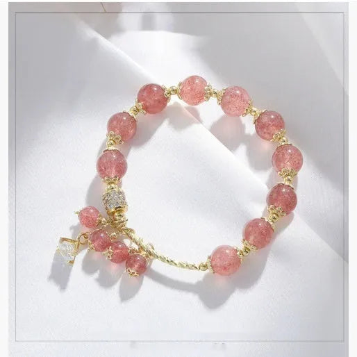 Close-up of a pink heart-shaped strawberry quartz crystal bracelet with pearl details on a wrist.