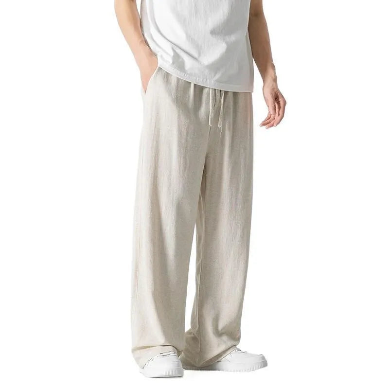 Men's beige loose-fit straight-leg linen trousers with drawstring waist, shown on a model.
