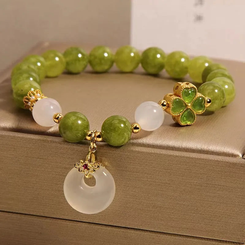 Women's green tourmaline bracelet with four-leaf clover safety buckle on a wrist.