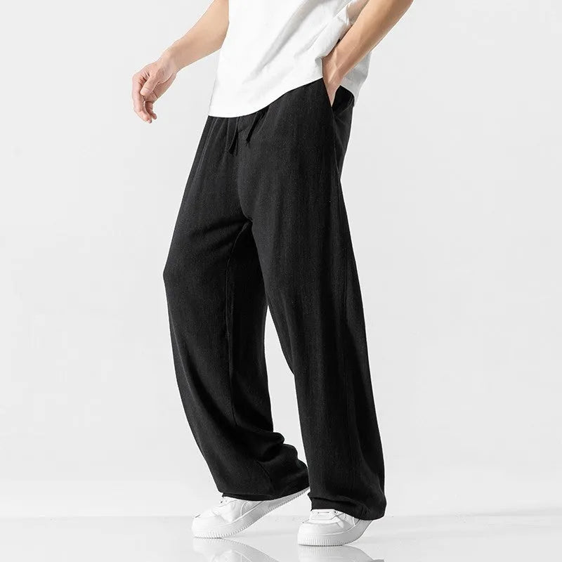 Men's beige loose-fit straight-leg linen trousers with drawstring waist, shown on a model.