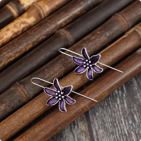 A pair of simple purple flower-shaped alloy earrings for women on a white background.