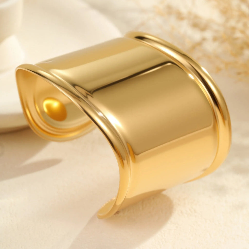 Gold-plated stainless steel bracelet with asymmetric geometric wave design and wide opening.
