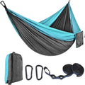 Green and camel parachute cloth hammock hung between two trees with black buckles and ropes.