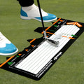 Black neoprene golf swing posture aid mat on grass, showing its compact size and alignment markings.