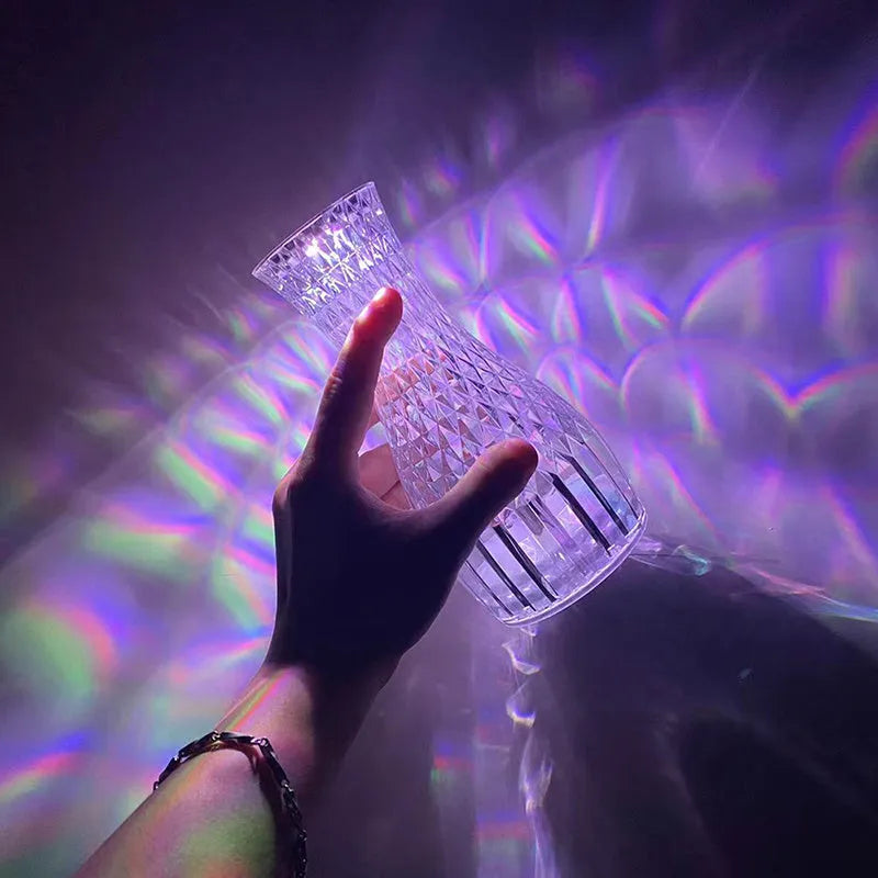 Vase-shaped transparent crystal table lamp with LED colour-changing lights on wooden surface