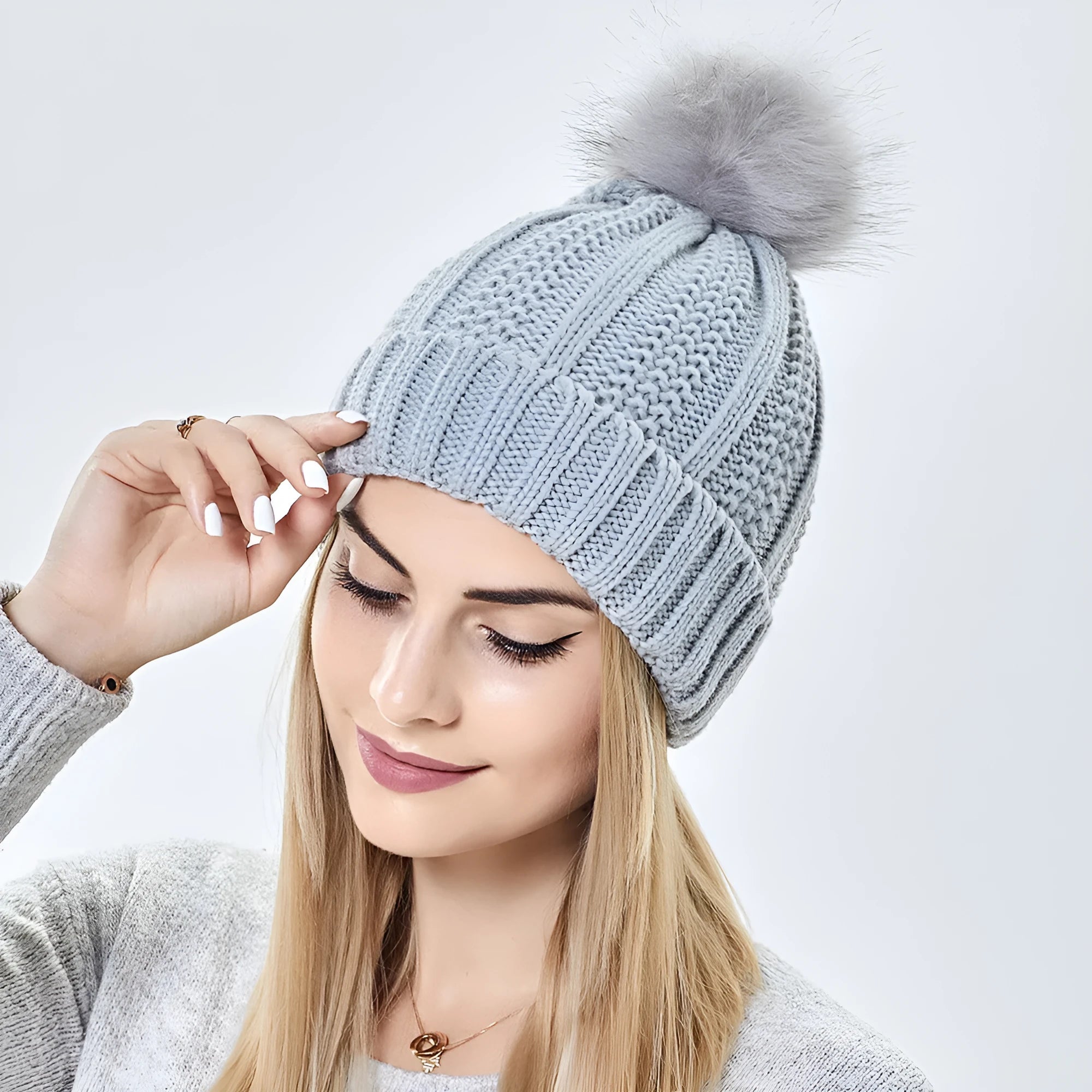 Women's knit beanie hat with a faux fur pom pom, shown in a beige colour, featuring a satin lining.