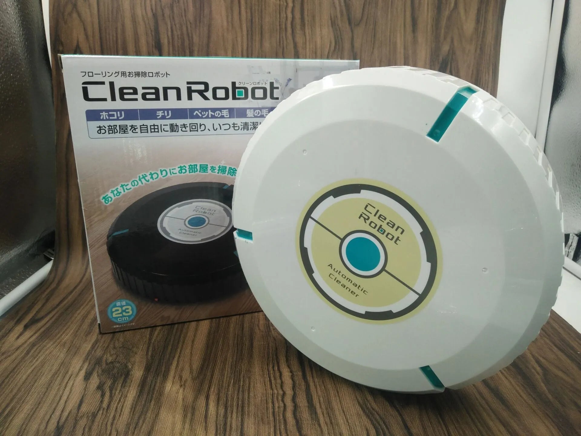 Black or white AC robot vacuum cleaner on a wooden floor showing its 23-inch square size and low profile.