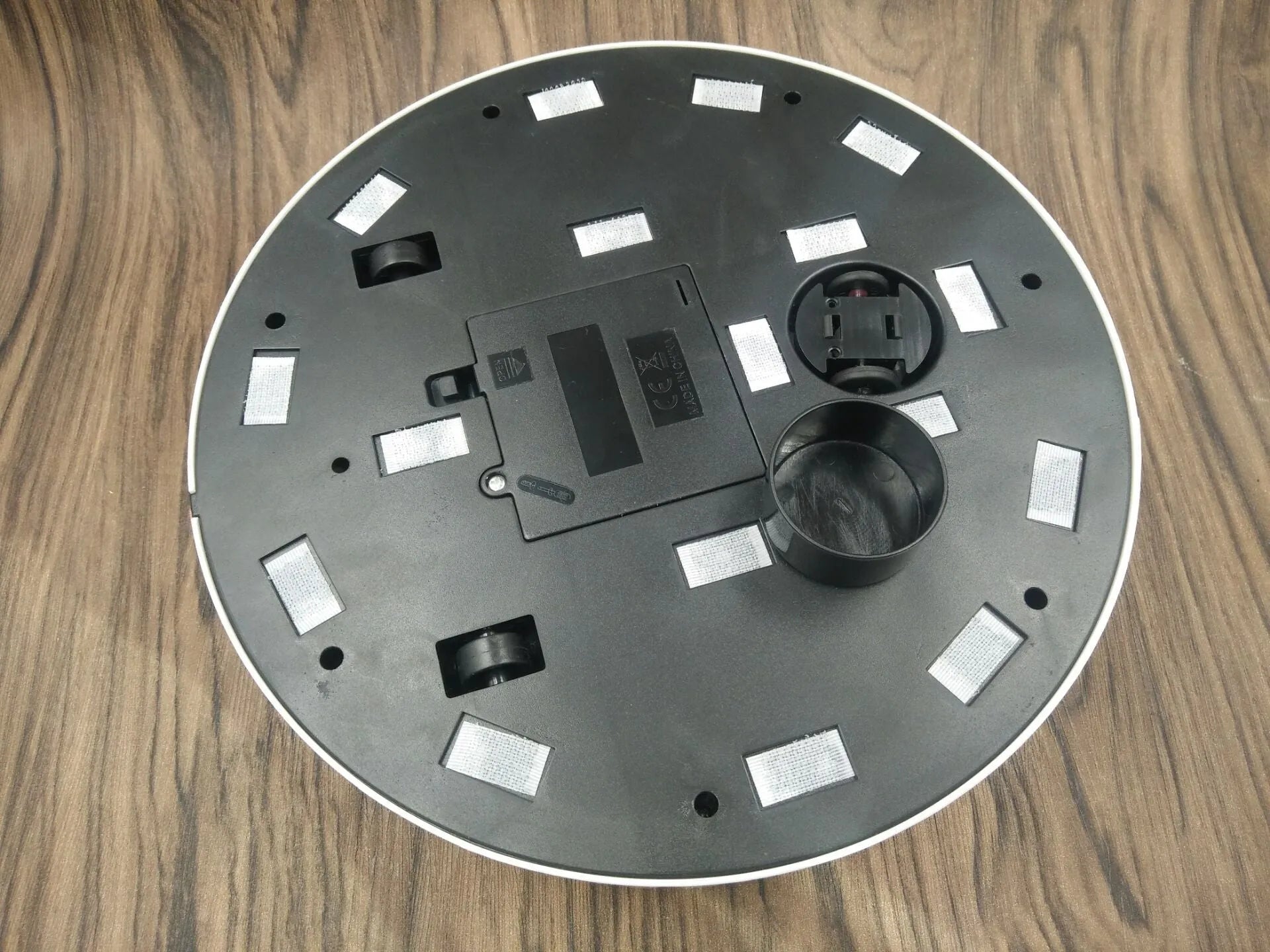 Black or white AC robot vacuum cleaner on a wooden floor showing its 23-inch square size and low profile.