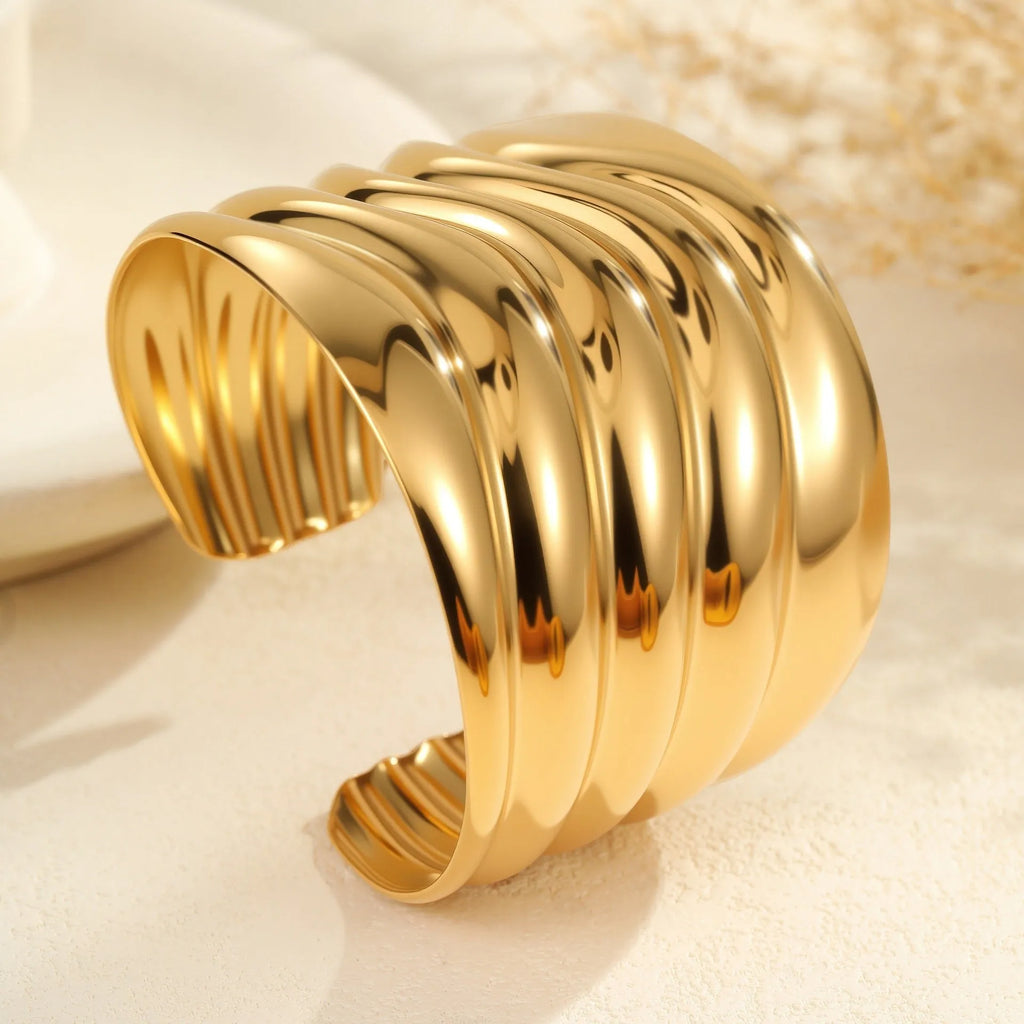 Gold-plated stainless steel bracelet with asymmetric geometric wave design and wide opening.