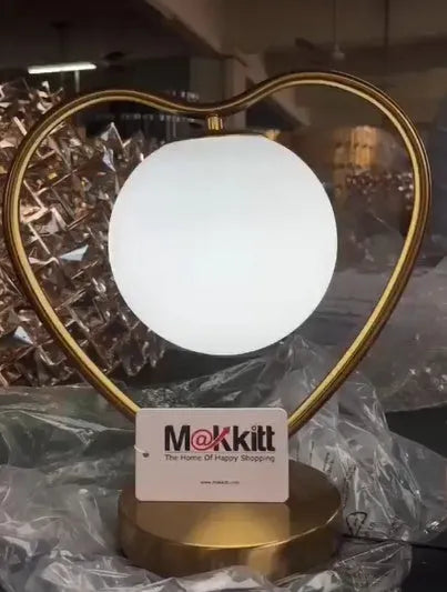 White heart shaped LED table lamp with transparent shade on a wooden surface.