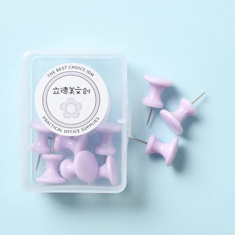 Box of coloured plastic push pins in cherry blossom pink, mint green and lavender on a white surface