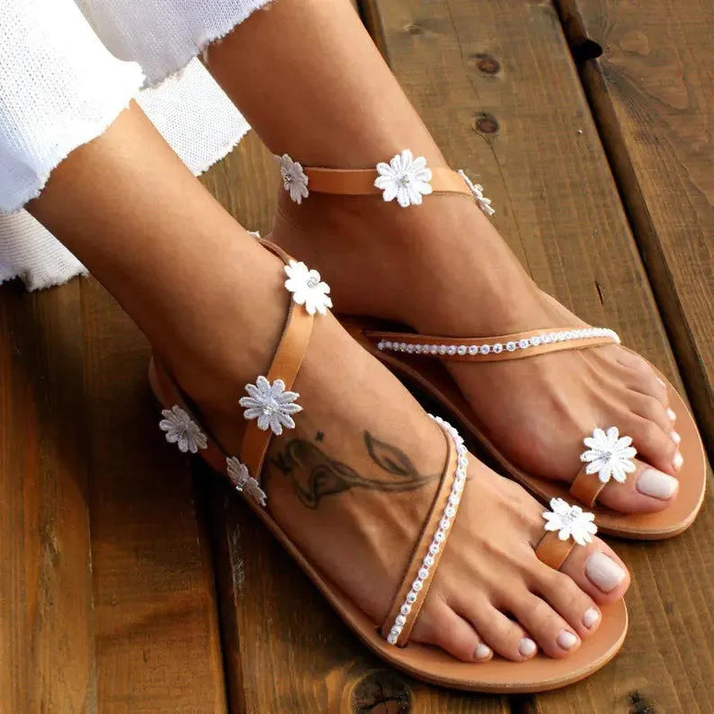 Brown women's Roman-style sandals with floral detail on the upper and a flat rubber sole.