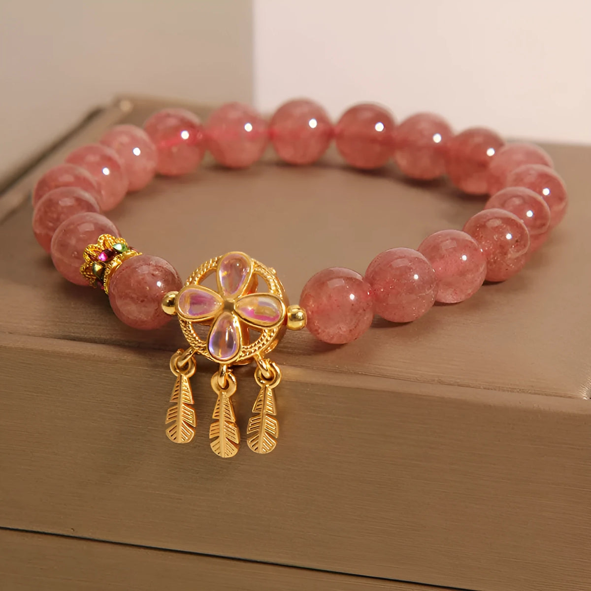 Women's strawberry quartz bracelet with four-leaf dream catcher ball pendant on wrist