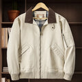 Men's beige washed cotton baseball style flight jacket on a hanger, showing classic design.