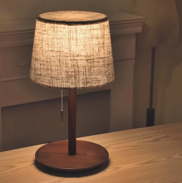 Walnut coloured solid wood bedside lamp with white cloth shade on a table.