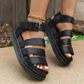 Black casual sandals with a buckle strap and thick rubber sole on a sandy beach