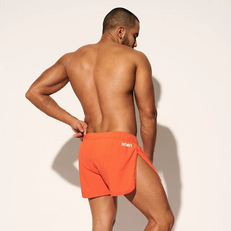 Man wearing loose orange red polyester beach surfing trousers on sand