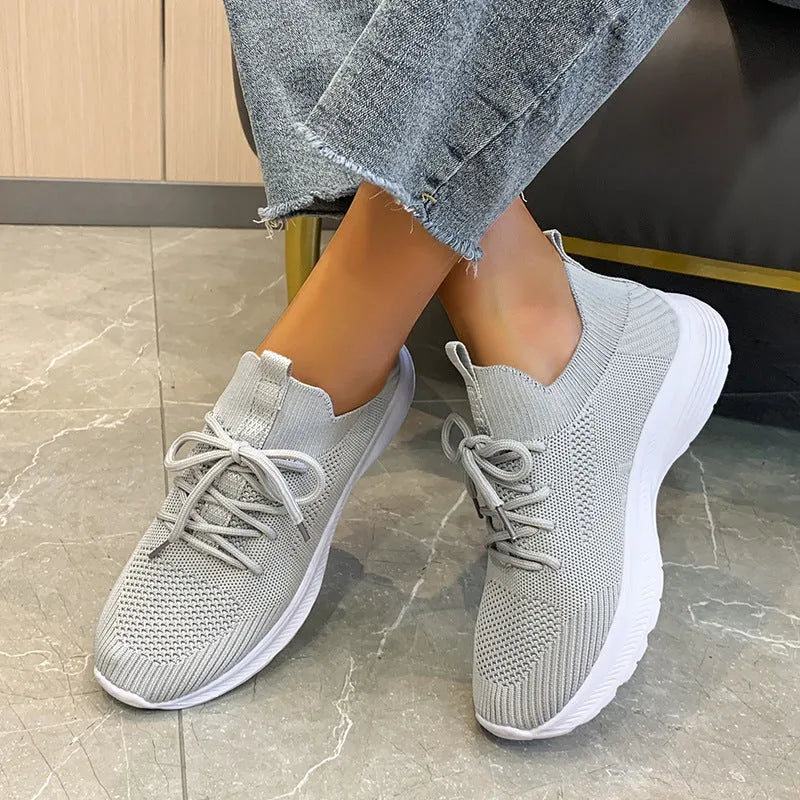 Women's creamy white low-top running shoes with a Flyknit upper and mesh detailing on a flat rubber sole.