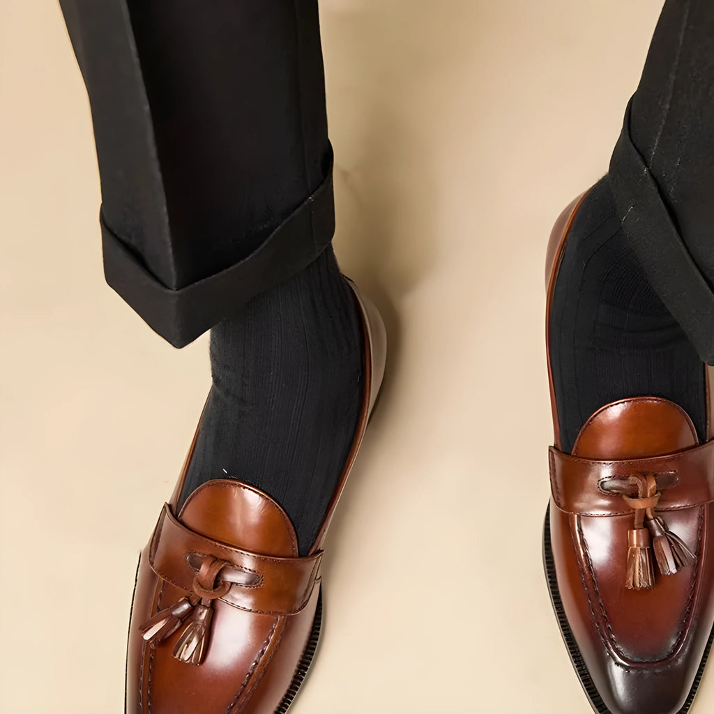 Men's black polished leather tassel loafers on a white background, side view showing rubber sole.