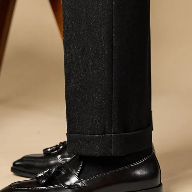 Men's black polished leather tassel loafers on a white background, side view showing rubber sole.