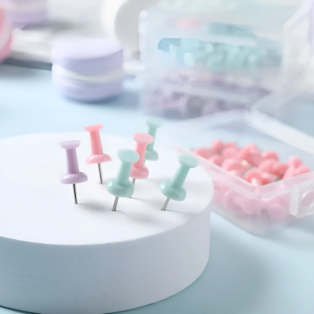 Box of coloured plastic push pins in cherry blossom pink, mint green and lavender on a white surface