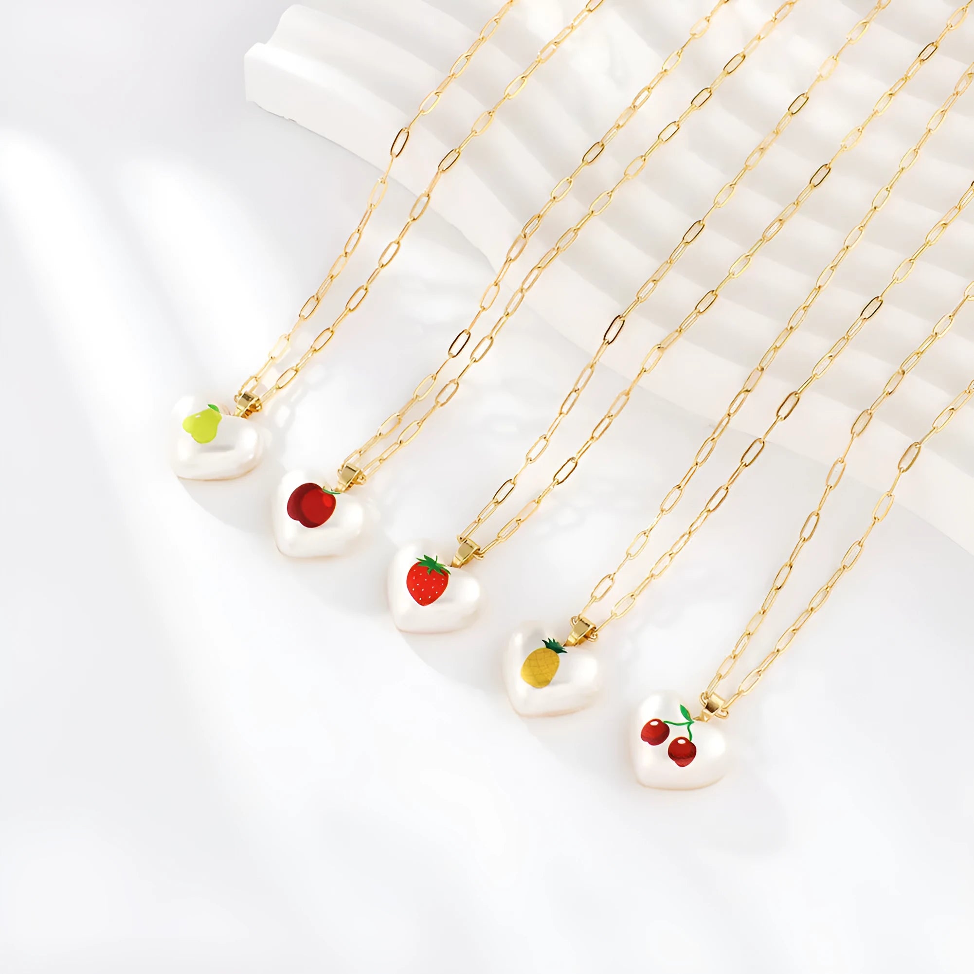 Adjustable heart necklace showing geometric fruit pendants: apple, pineapple, strawberry, cherry, and pear.