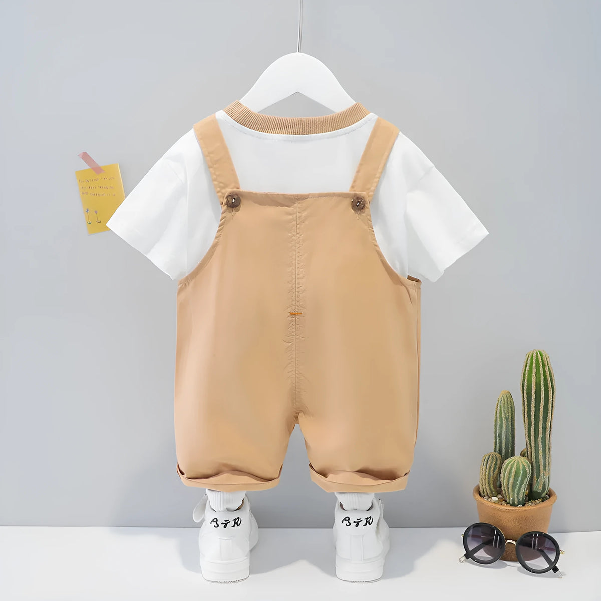 Yellow cartoon print short-sleeved baby overalls with adjustable straps on a hanger.