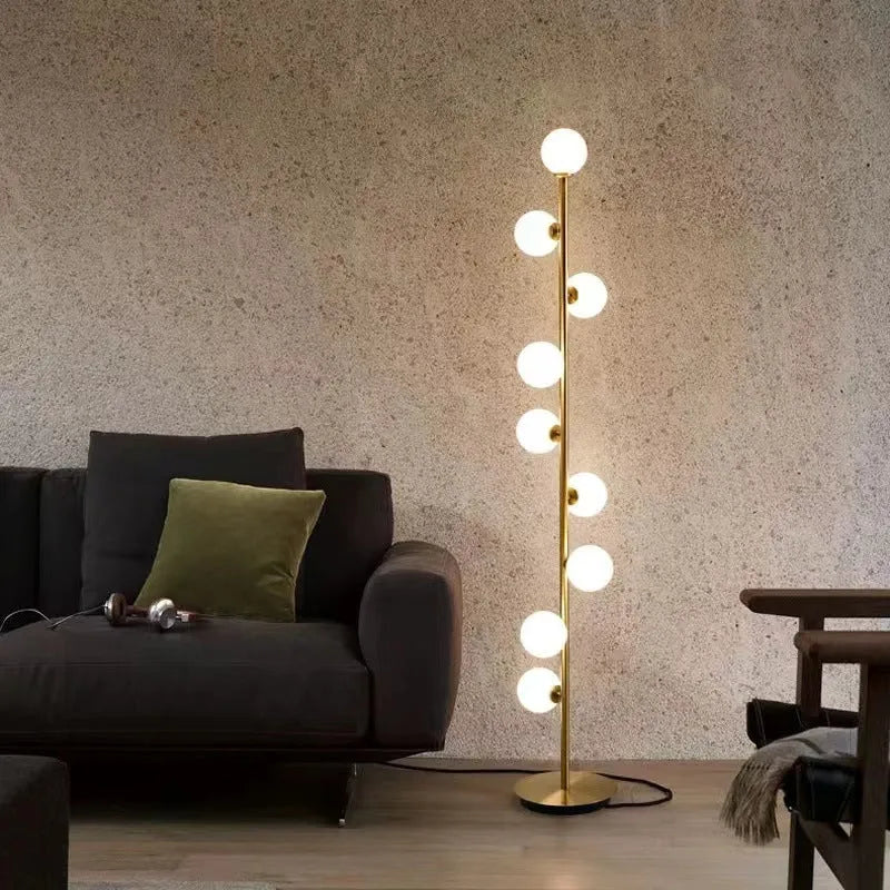 A tall, modern minimalist floor lamp with a wrought iron and glass body standing on a circular marble base.
