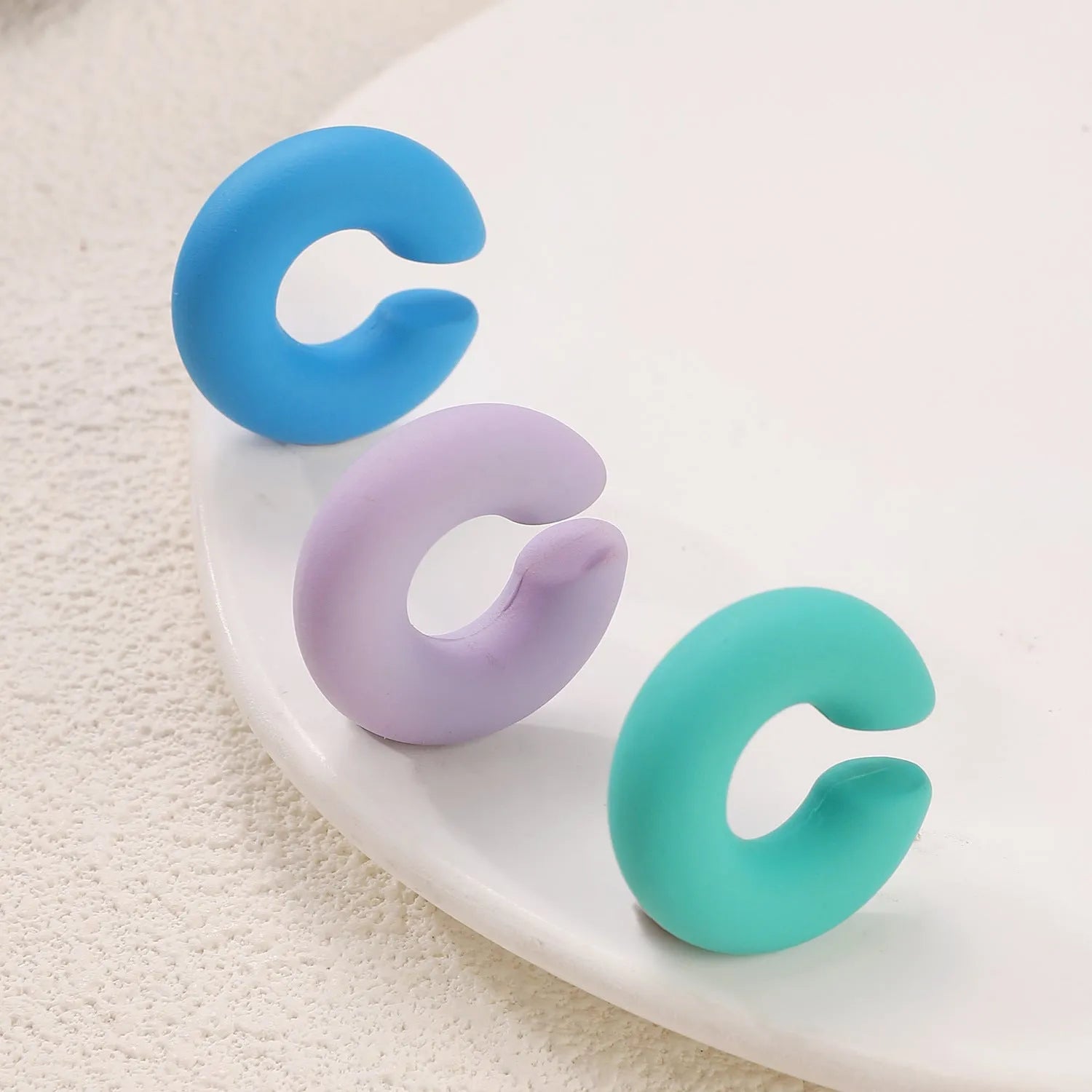 Geometric round C-shaped clip-on earrings in a matte coarse candy colour on a white background.