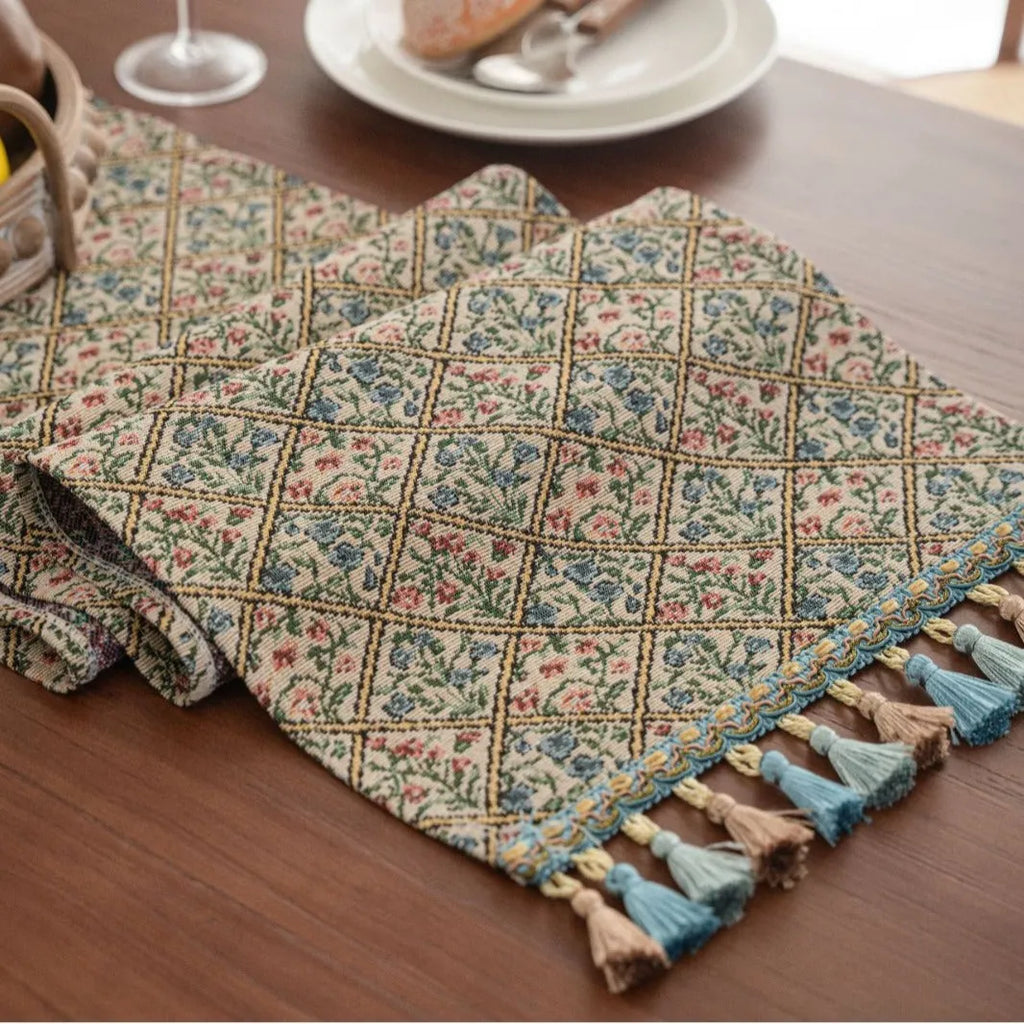 Dark blue striped table runner with jacquard bouquet pattern and tassel ends on a wooden table.