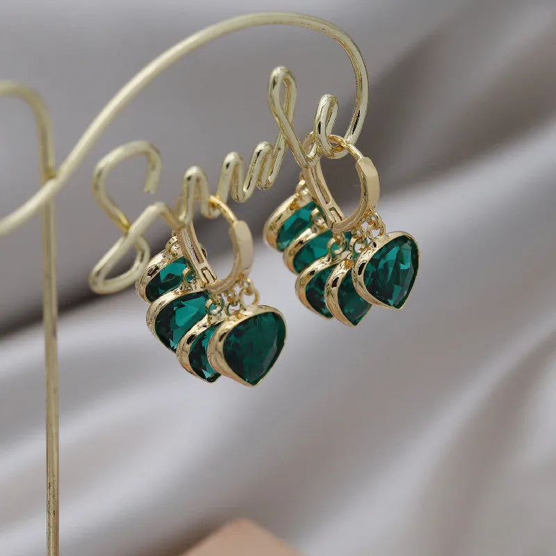 Pair of green heart-shaped glass pendant ear clip earrings with alloy inlay detail.