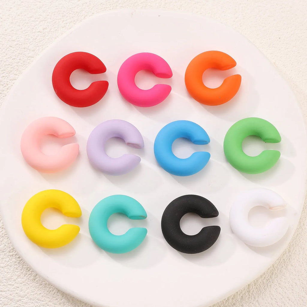 Geometric round C-shaped clip-on earrings in a matte coarse candy colour on a white background.