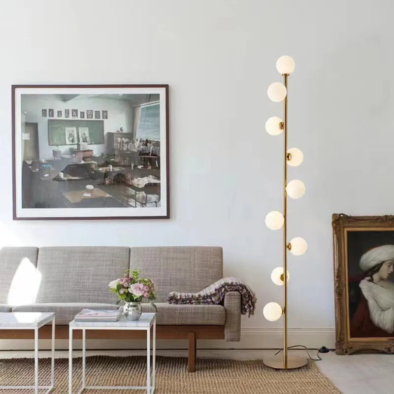 A tall, modern minimalist floor lamp with a wrought iron and glass body standing on a circular marble base.