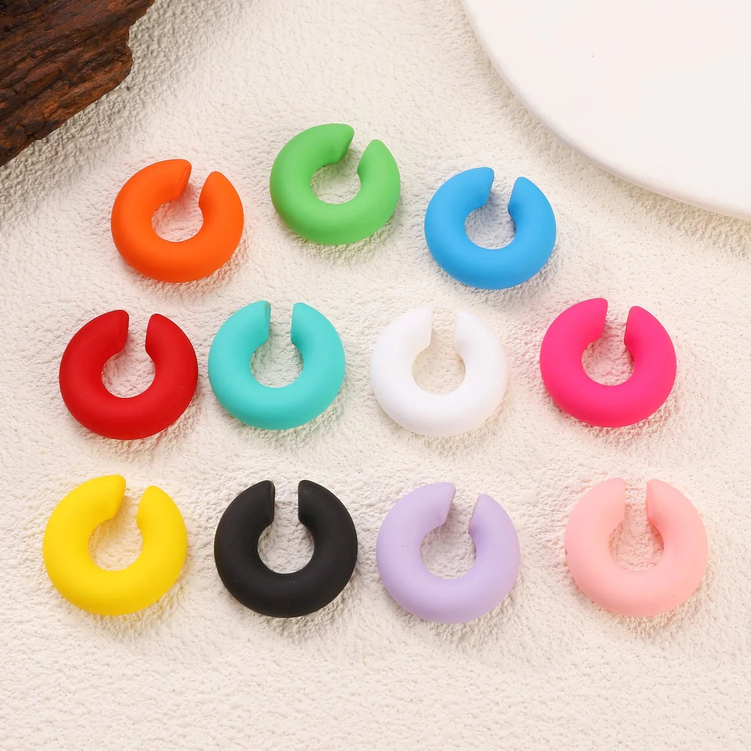 Geometric round C-shaped clip-on earrings in a matte coarse candy colour on a white background.