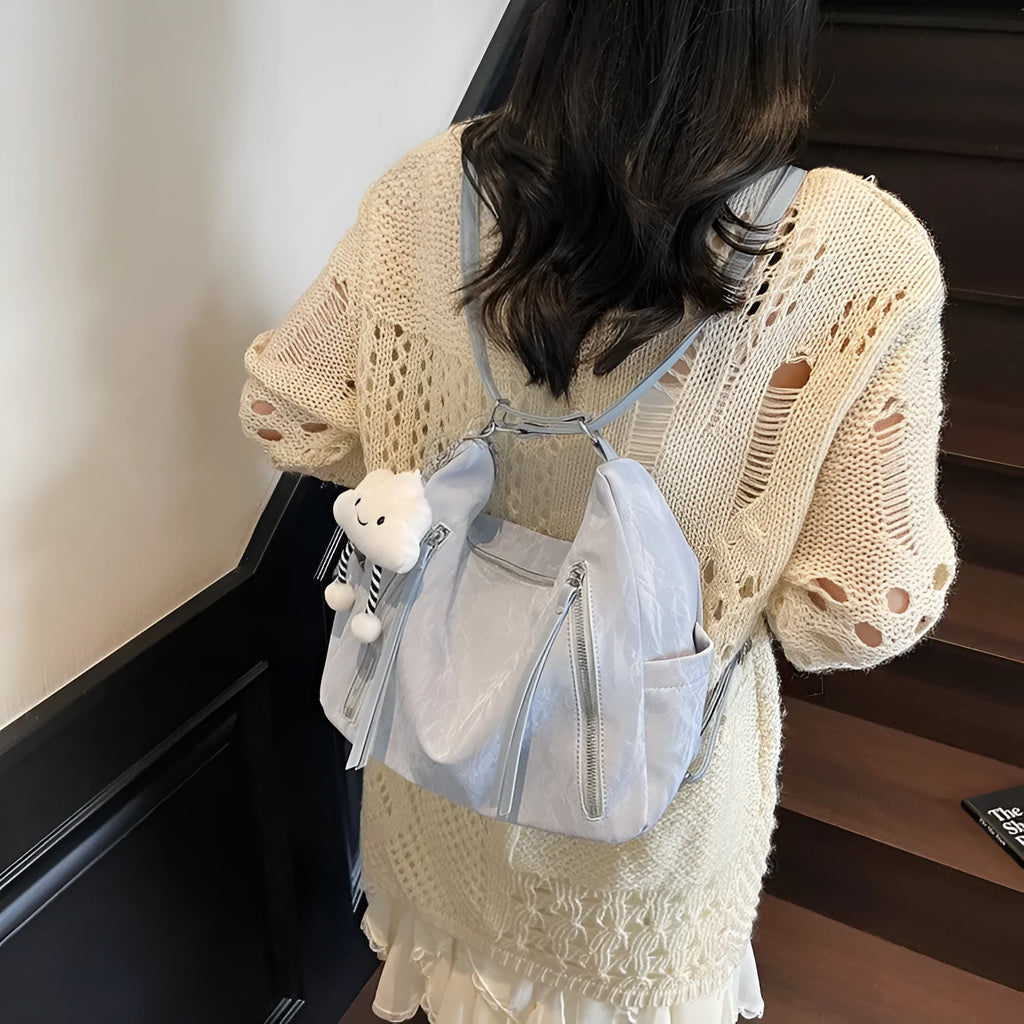 Women's soft black PU fashion backpack with a pendant accessory on a table.
