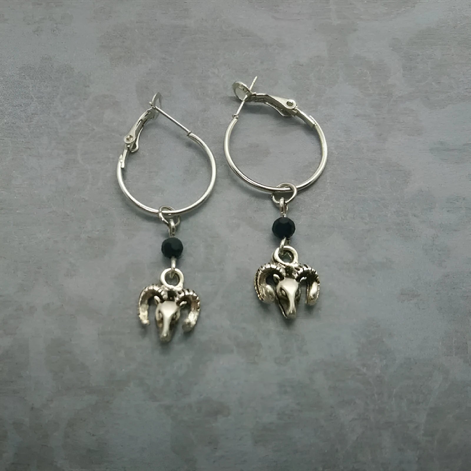 A pair of silver-coloured round hoop earrings with a detailed Tibetan antelope design.