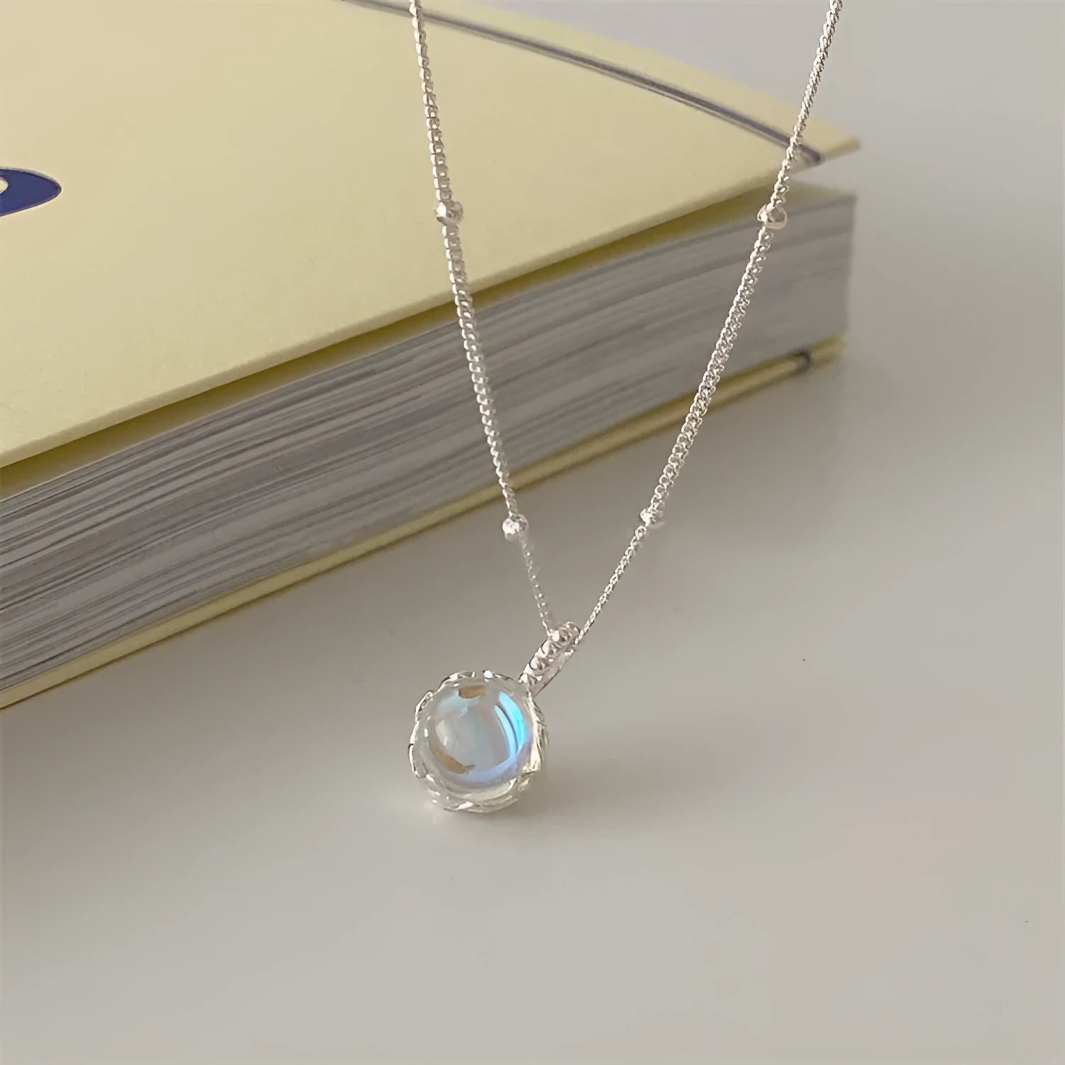Women's sterling silver curb chain necklace with a geometric ornamental stone pendant on a grey background.