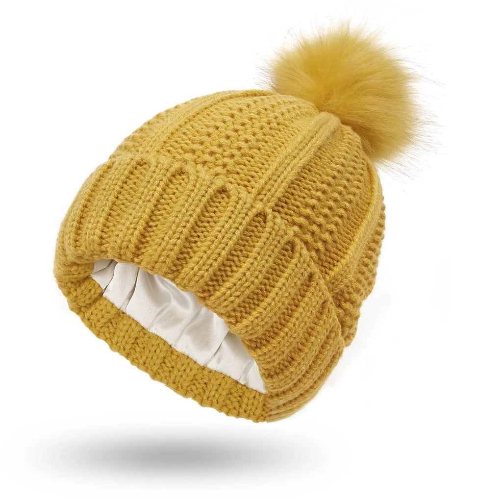 Women's knit beanie hat with a faux fur pom pom, shown in a beige colour, featuring a satin lining.