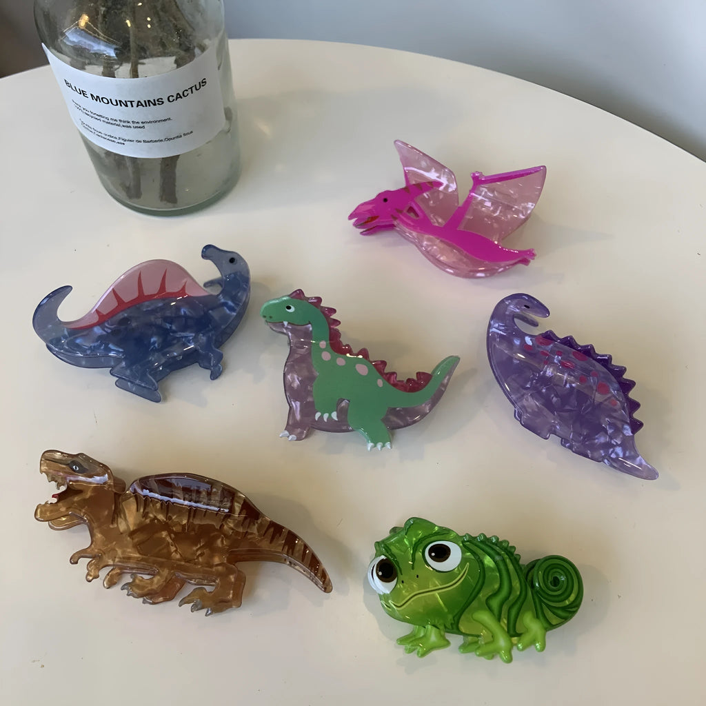 Acrylic dinosaur jaw hair clip showing six colour options including Pink Pterosaur and Blue Little Dinosaur designs